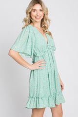 woman wearing a sage green floral mini dress with flutter sleeves and a ruffled hem