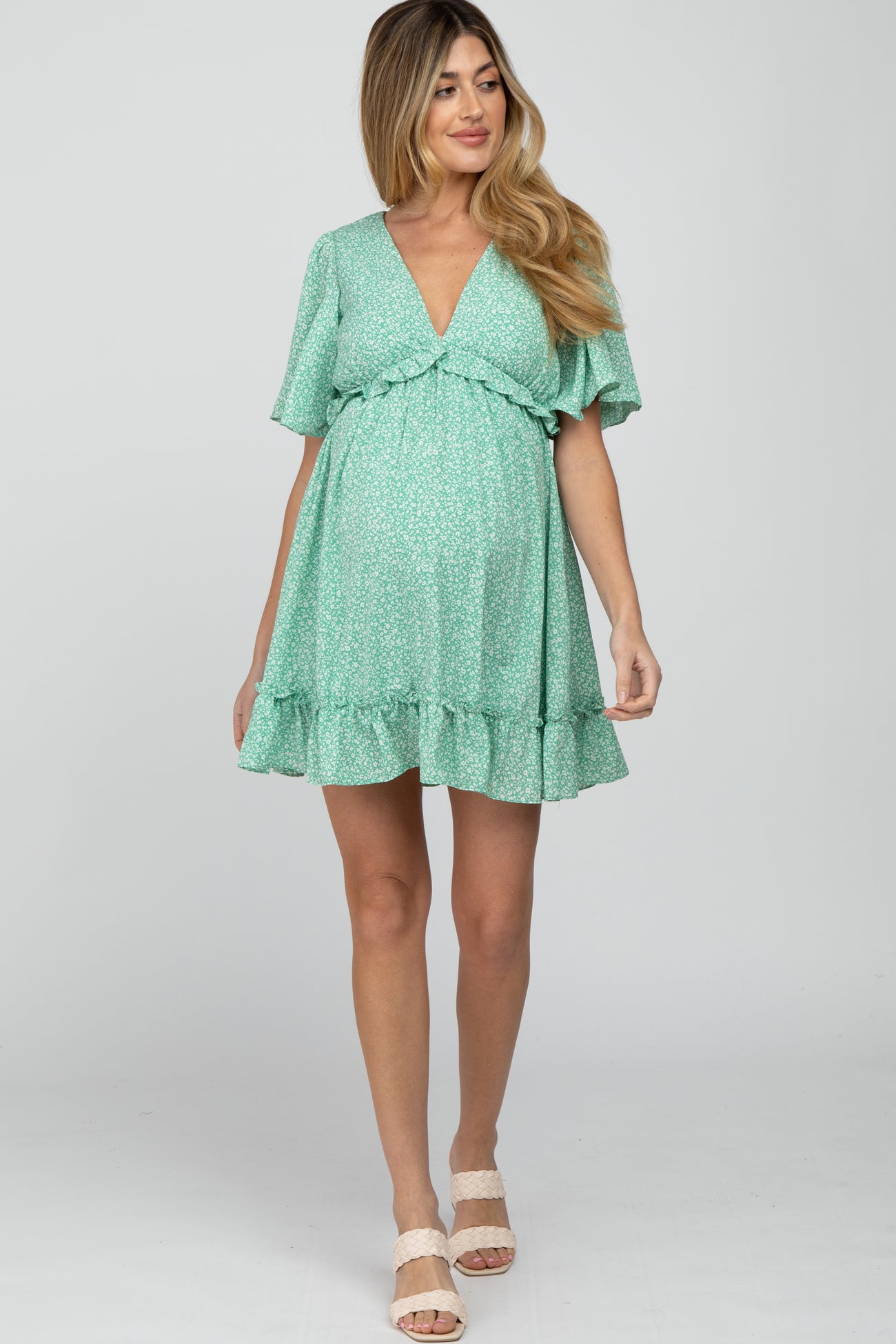 pregnant woman wearing a mint green floral maternity mini dress with a v-neckline and ruffle hem
