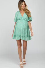 pregnant woman wearing a mint green floral maternity mini dress with a v-neckline and ruffle hem