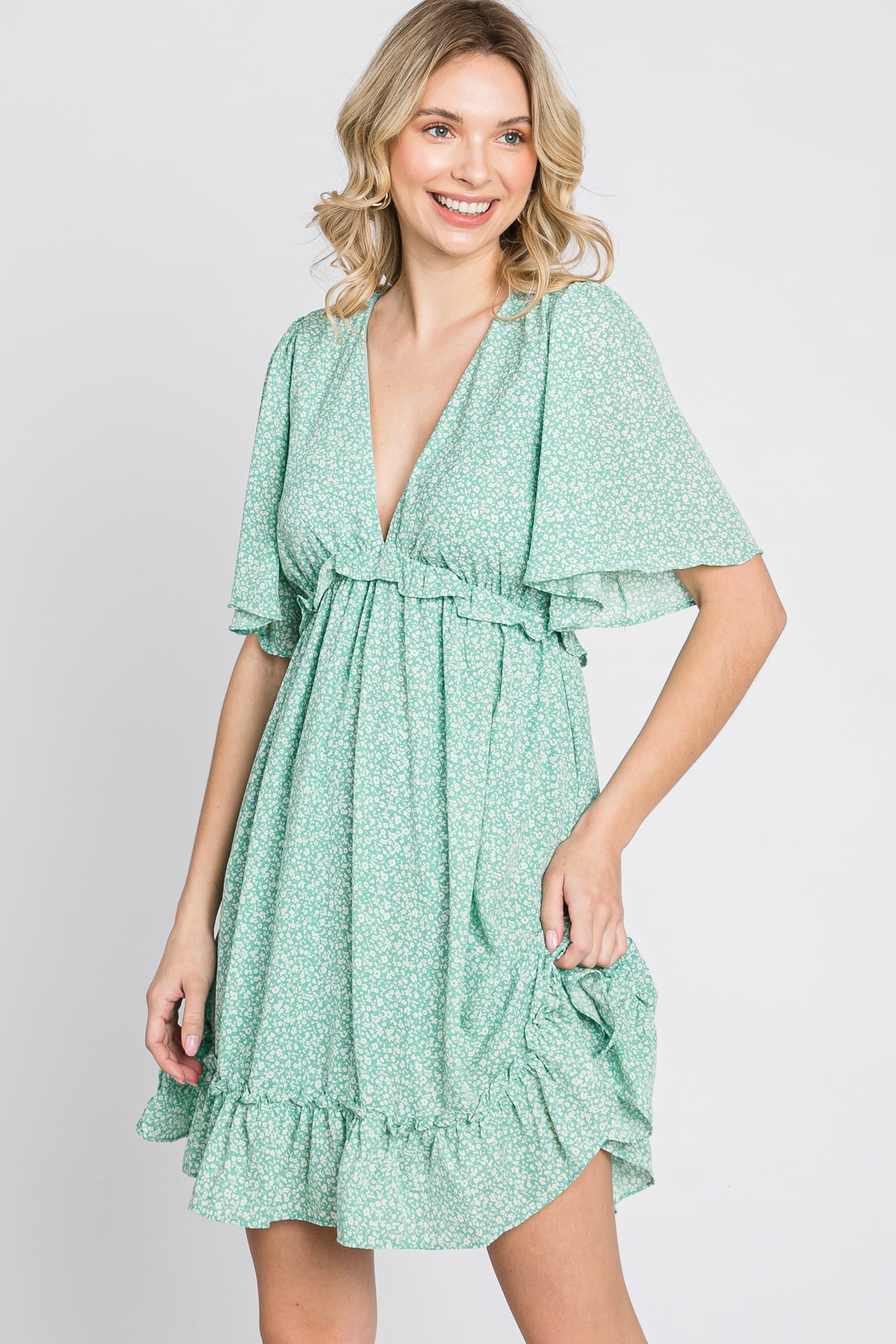 smiling woman wearing a green floral v-neck mini dress with flutter sleeves and ruffle hem