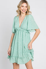 smiling woman wearing a green floral v-neck mini dress with flutter sleeves and ruffle hem