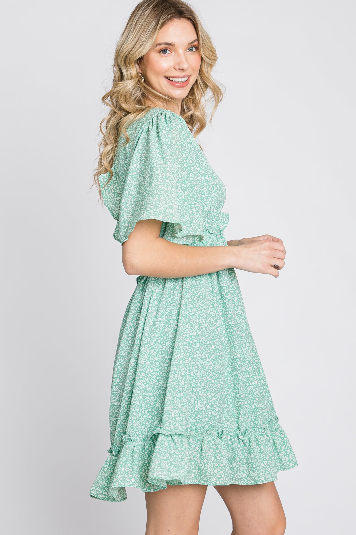 woman wearing a green floral print mini dress with flutter sleeves and a ruffled hem