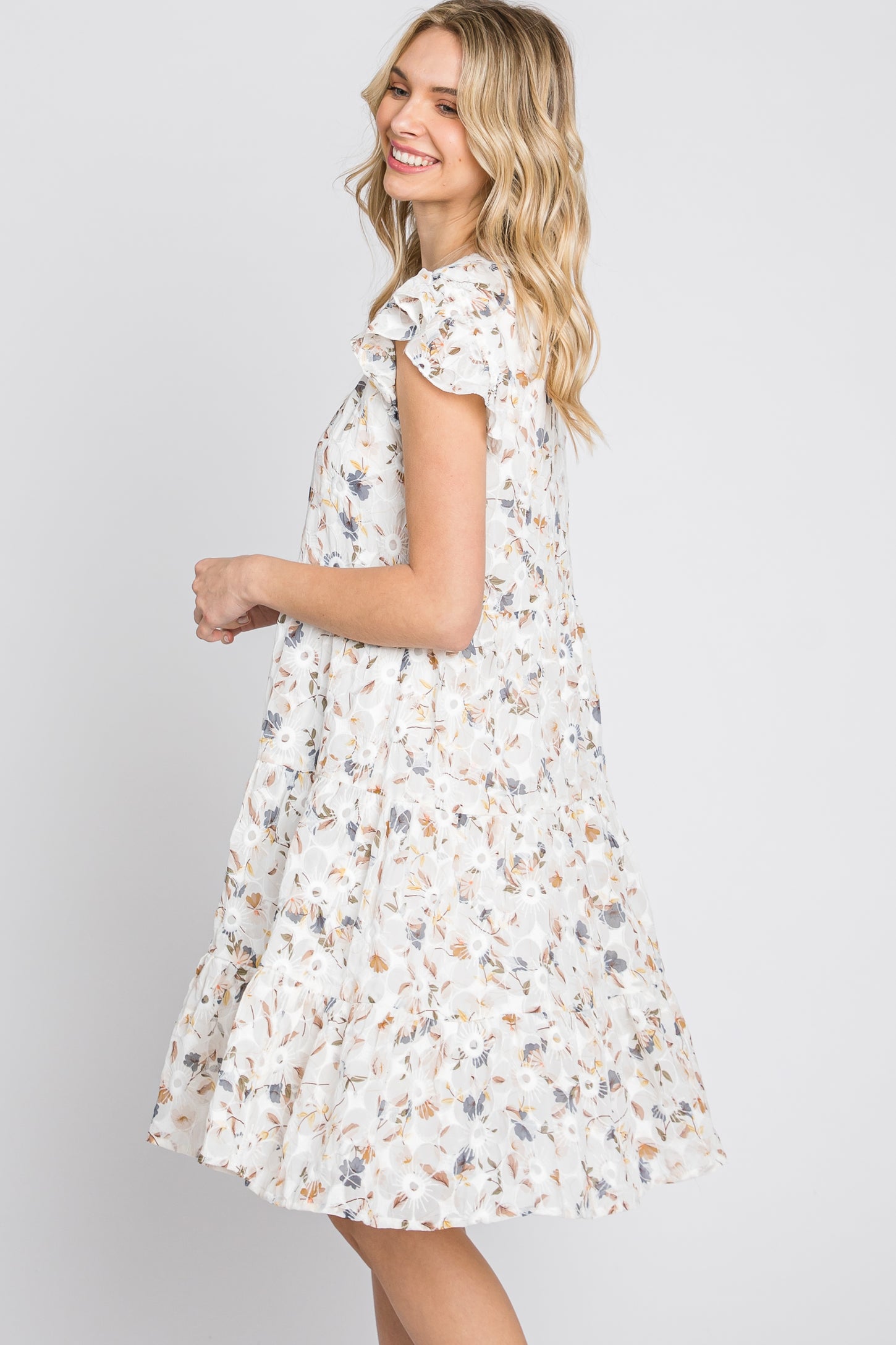 smiling woman wearing a white floral tiered babydoll dress with ruffle sleeves against a white background