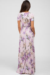 Back view of a woman wearing a light pink short sleeve floral maxi dress with purple and tan flowers