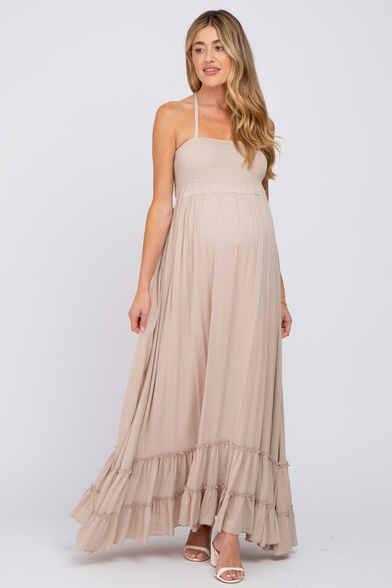 pregnant woman wearing a beige smocked halter maternity maxi dress with ruffle hem and white heels