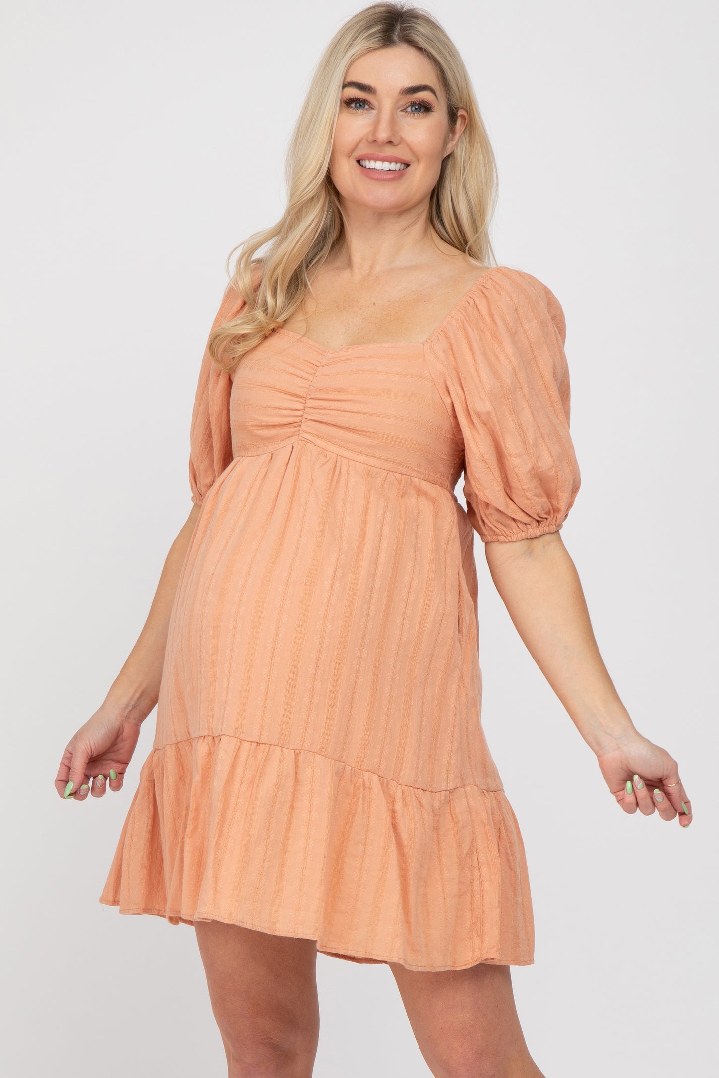 pregnant woman wearing a peach puff sleeve maternity mini dress with a ruffled hem