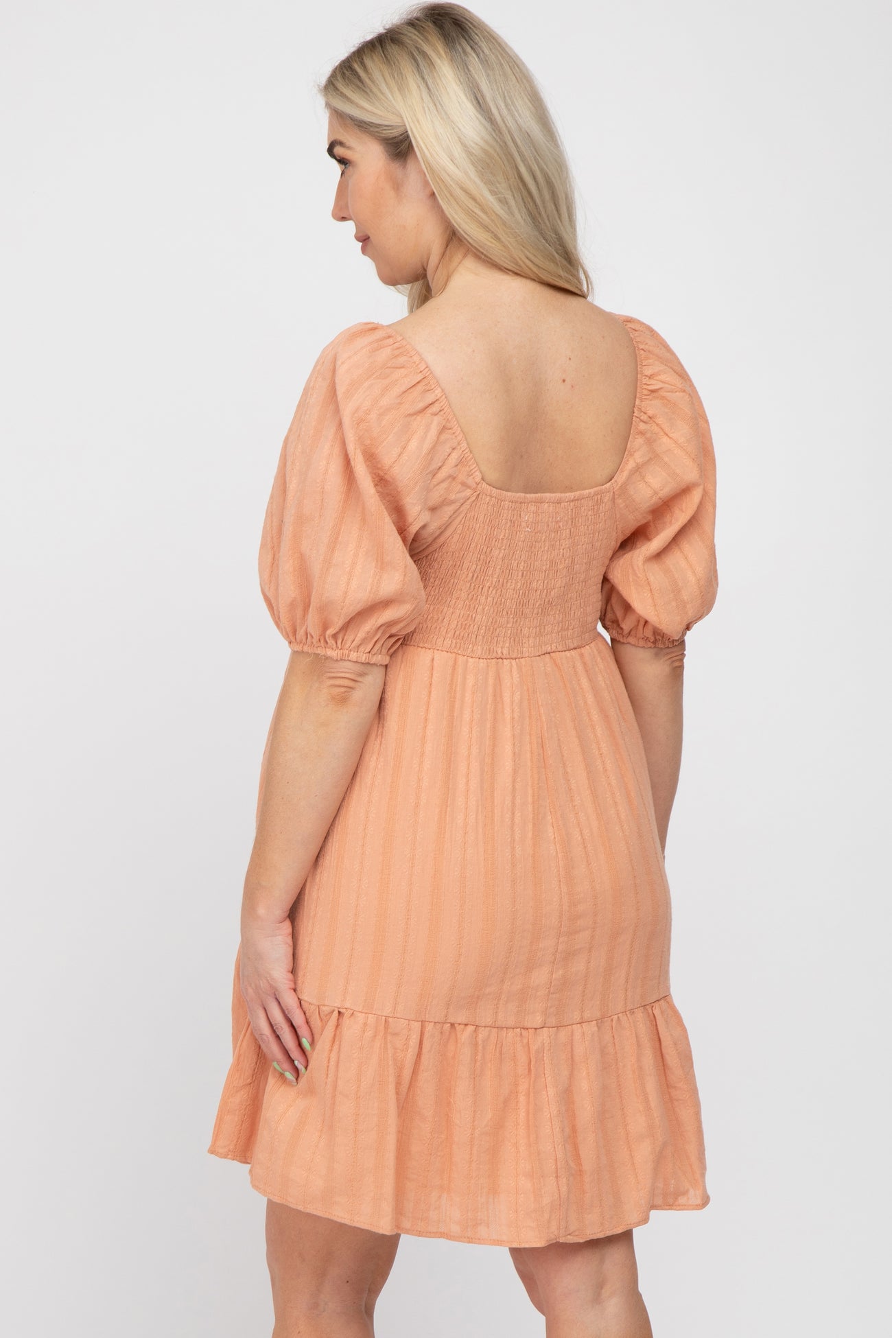 Back view of a woman wearing a peach puff sleeve dress with a smocked back and tiered skirt