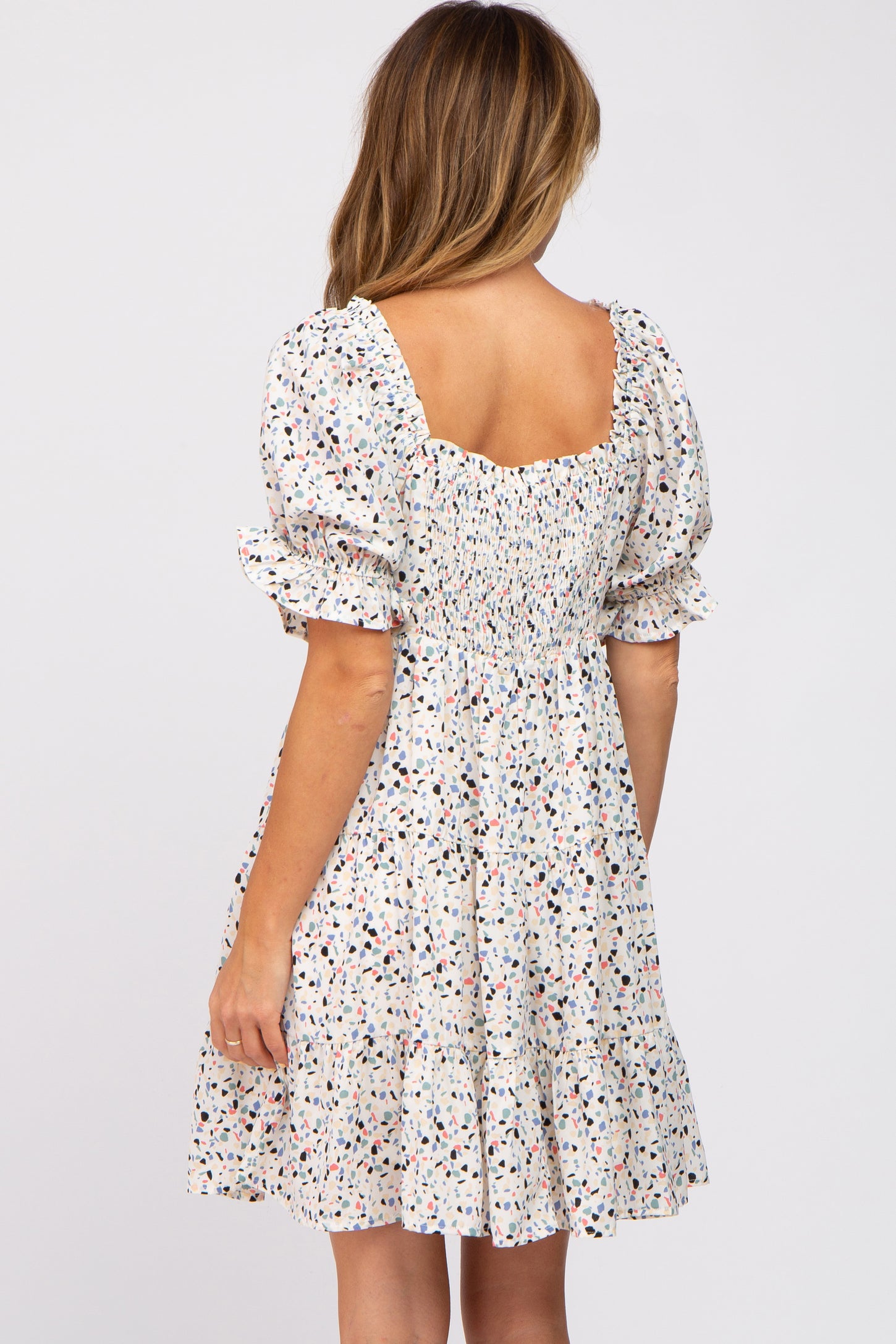 Back view of woman wearing a white smocked mini dress with colorful terrazzo print and puff sleeves
