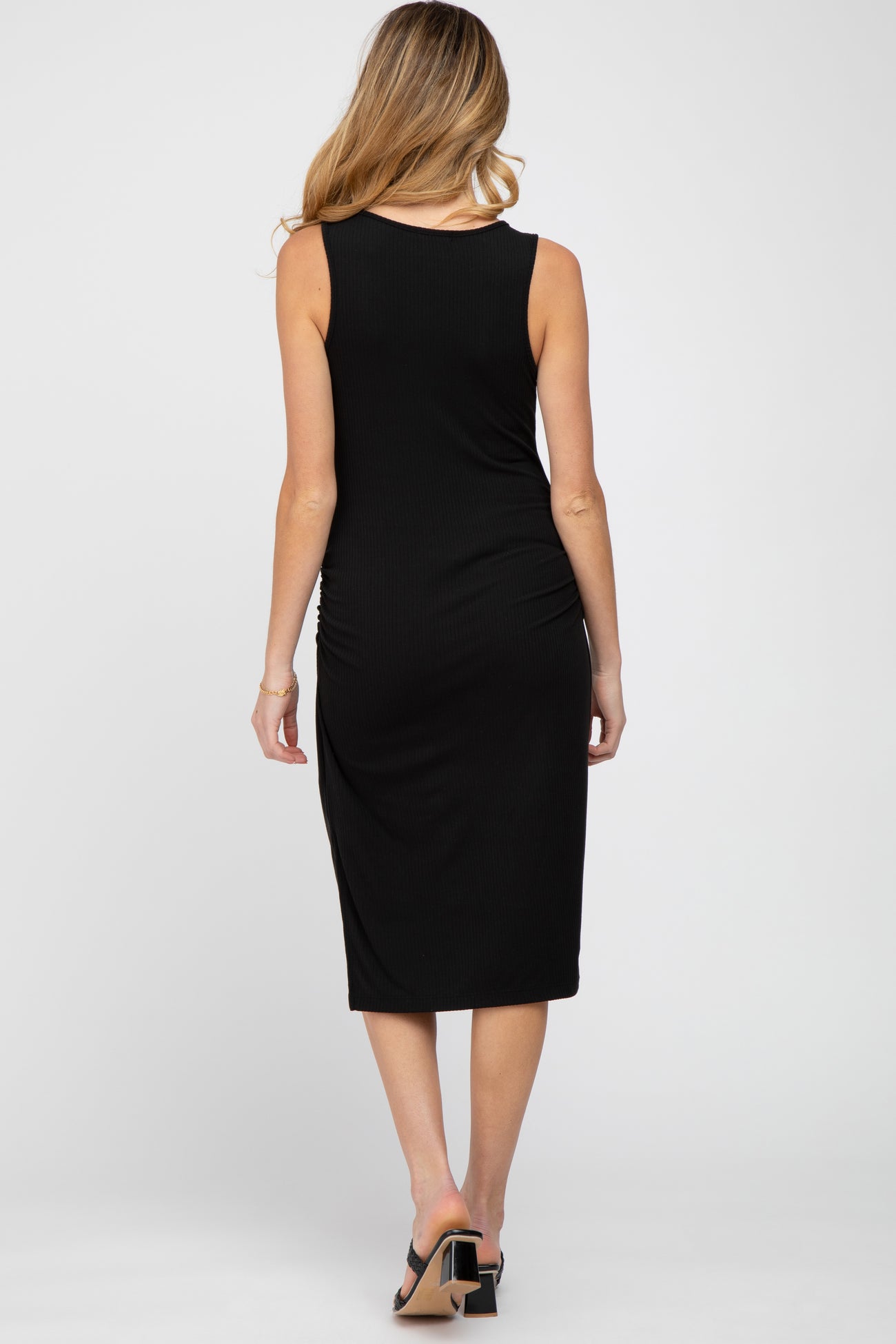 back view of a woman wearing a sleeveless black ribbed midi dress and black block heel sandals