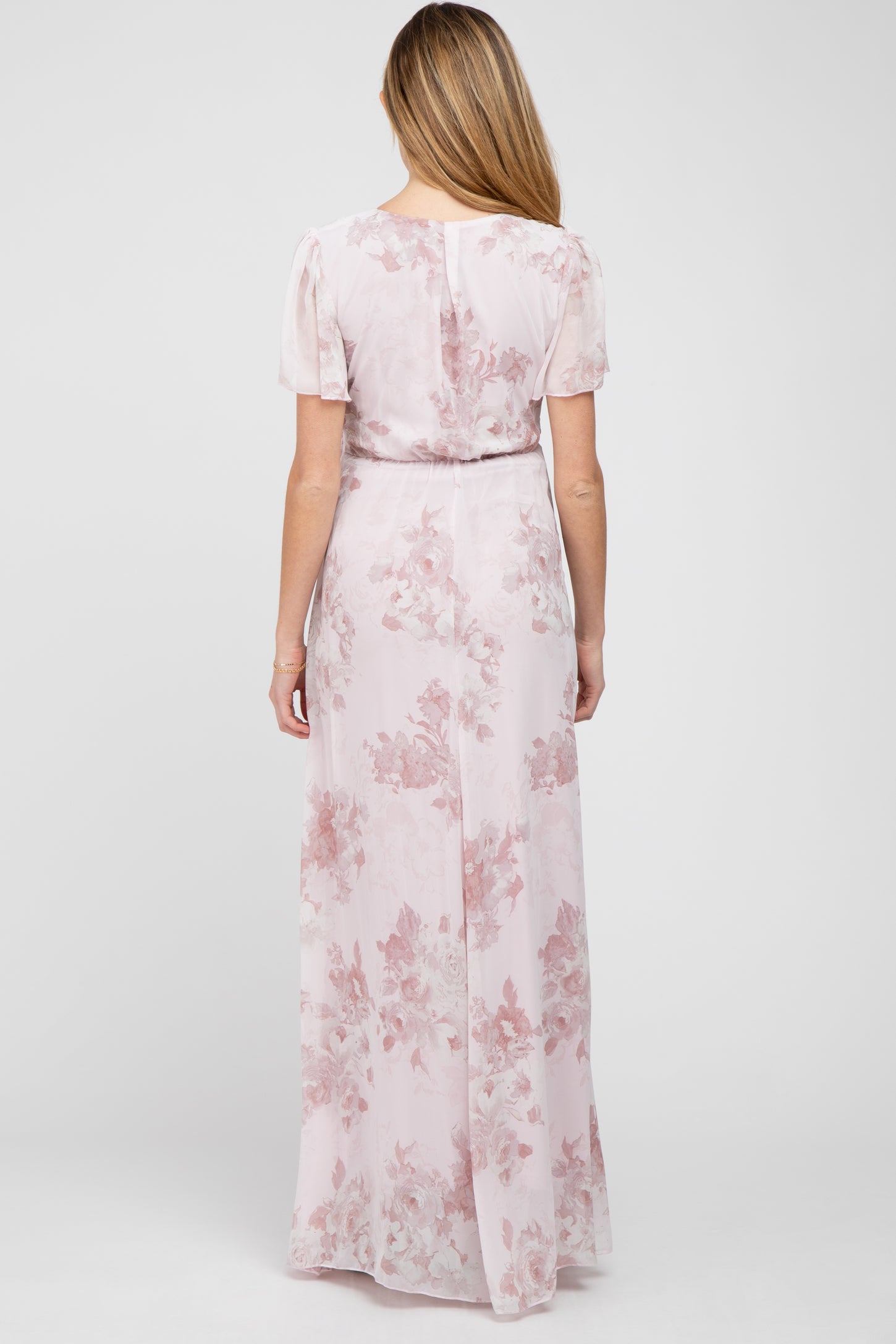 Back view of a woman wearing a light pink floral maxi dress with short flutter sleeves