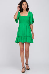 woman wearing a short green smocked dress with flutter sleeves and black strappy heels