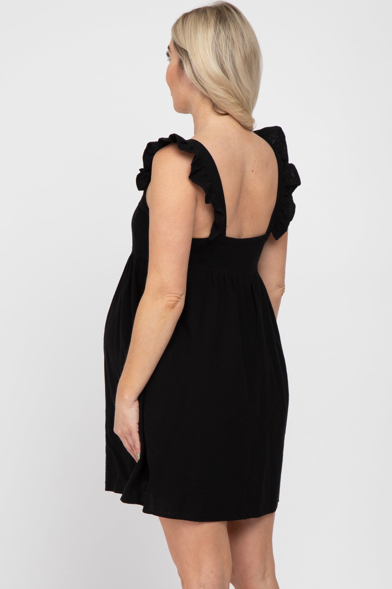 Pregnant woman wearing a black maternity dress with ruffle straps and an open back design