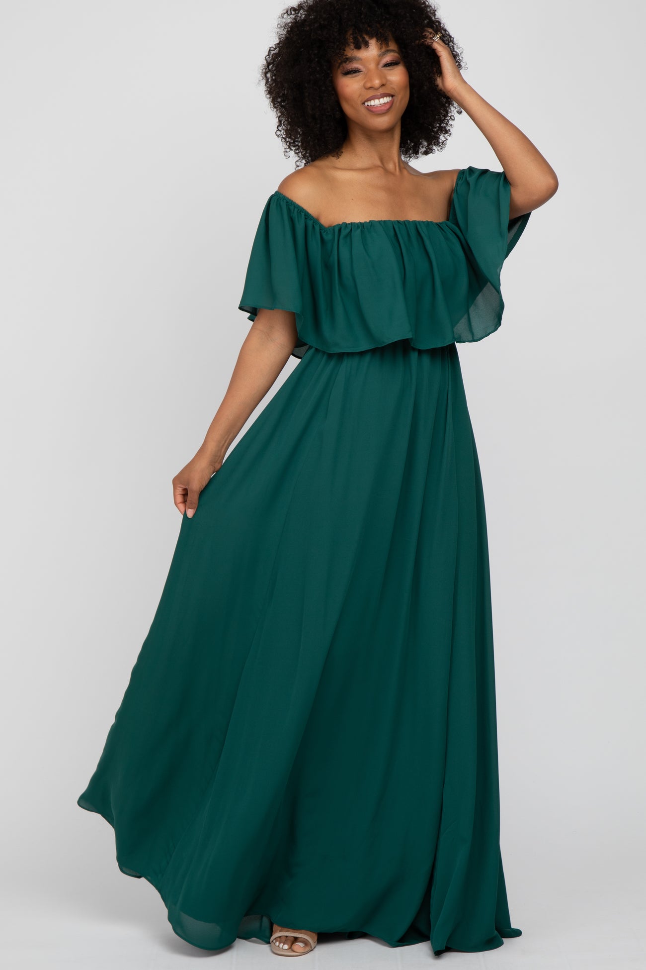 woman with curly hair wearing an off-the-shoulder emerald green maxi dress with a ruffled neckline