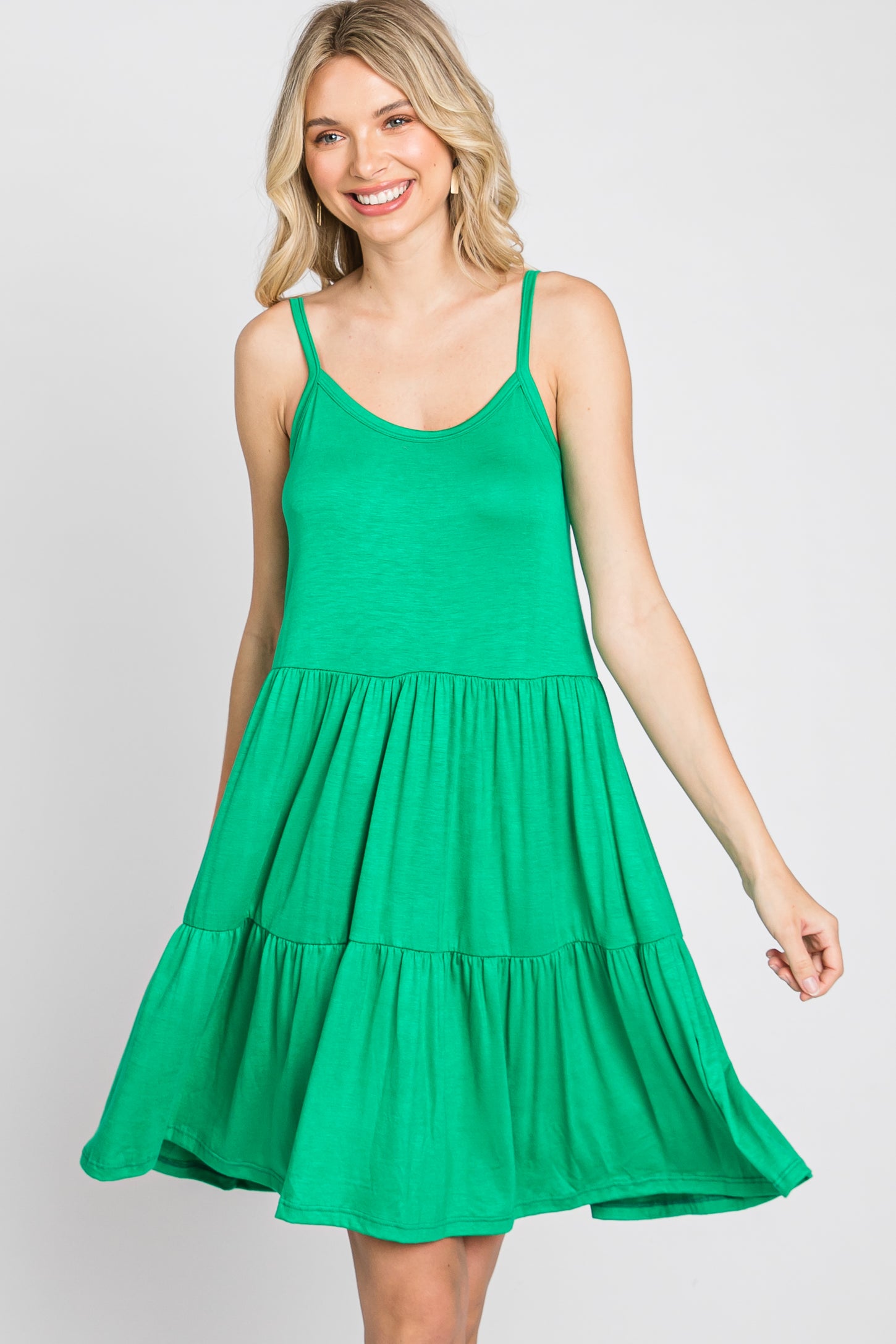 Woman wearing a green sleeveless tiered mini dress with spaghetti straps against a white background