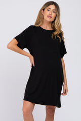 woman wearing a black short sleeve maternity t-shirt dress with a front pocket against a white background