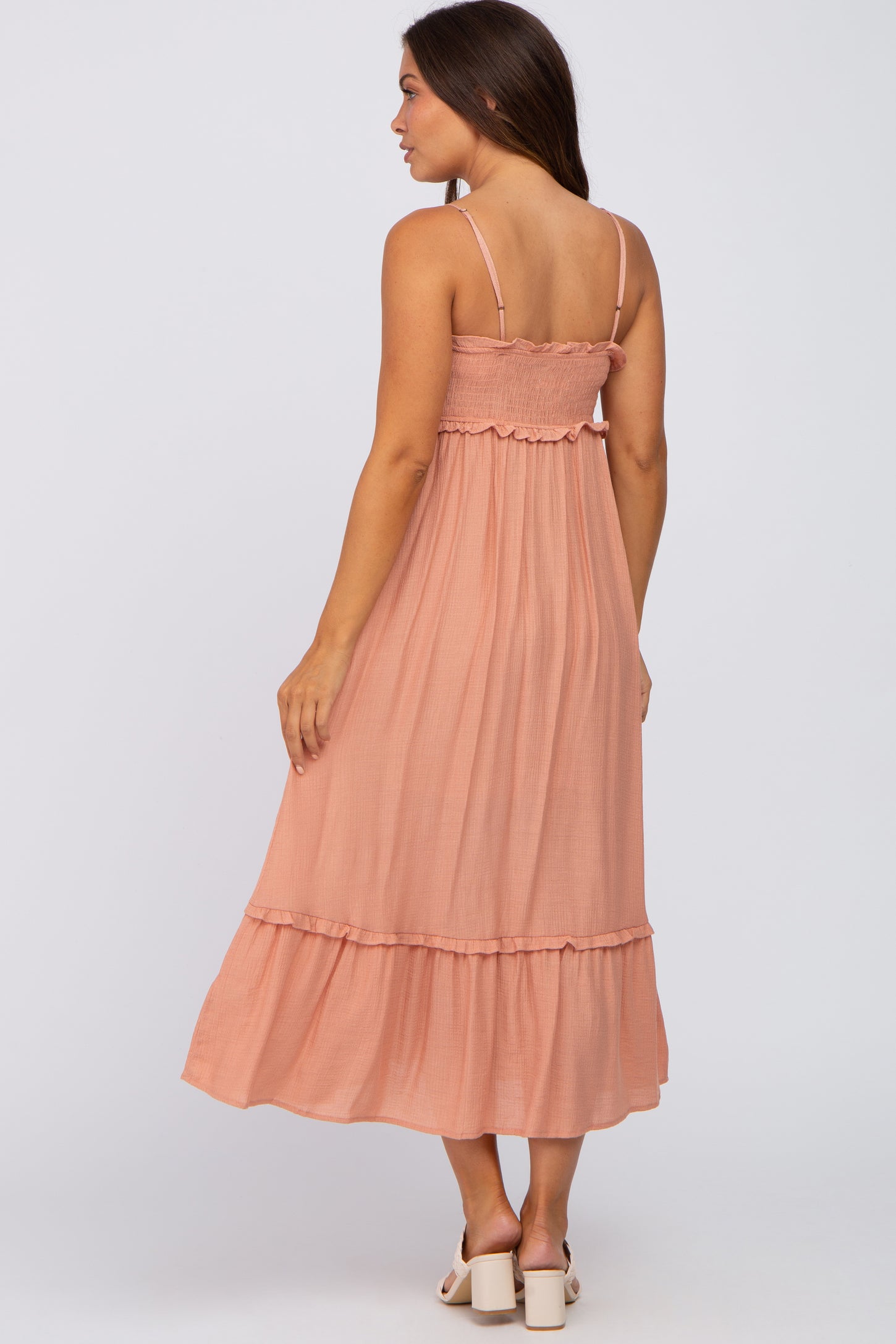 woman wearing a peach smocked maternity midi dress with ruffle trim and spaghetti straps