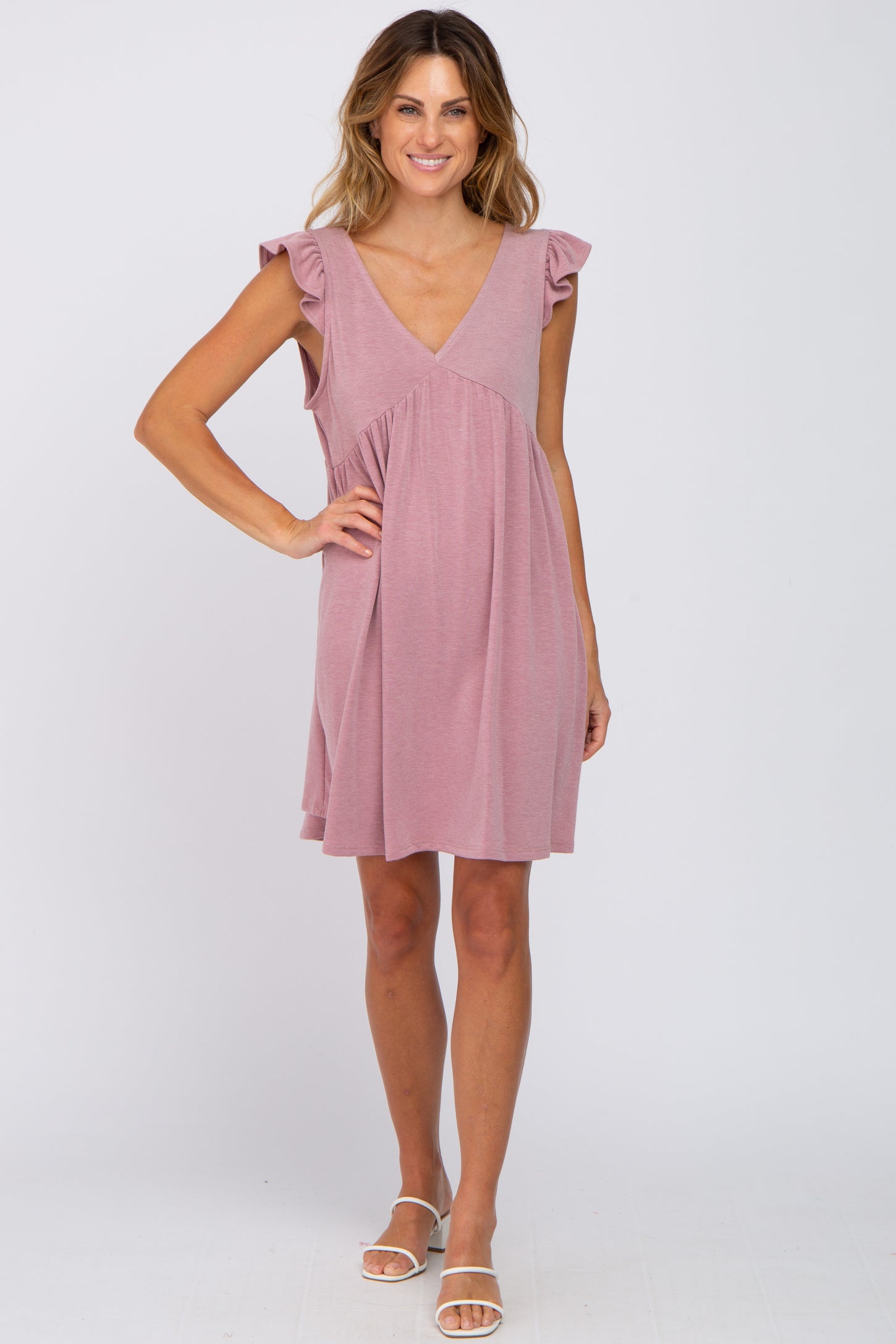 woman wearing a mauve v-neck ruffle sleeve maternity dress with white sandals