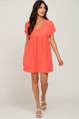 woman wearing a coral pink swiss dot v-neck babydoll dress with short sleeves and white sandals