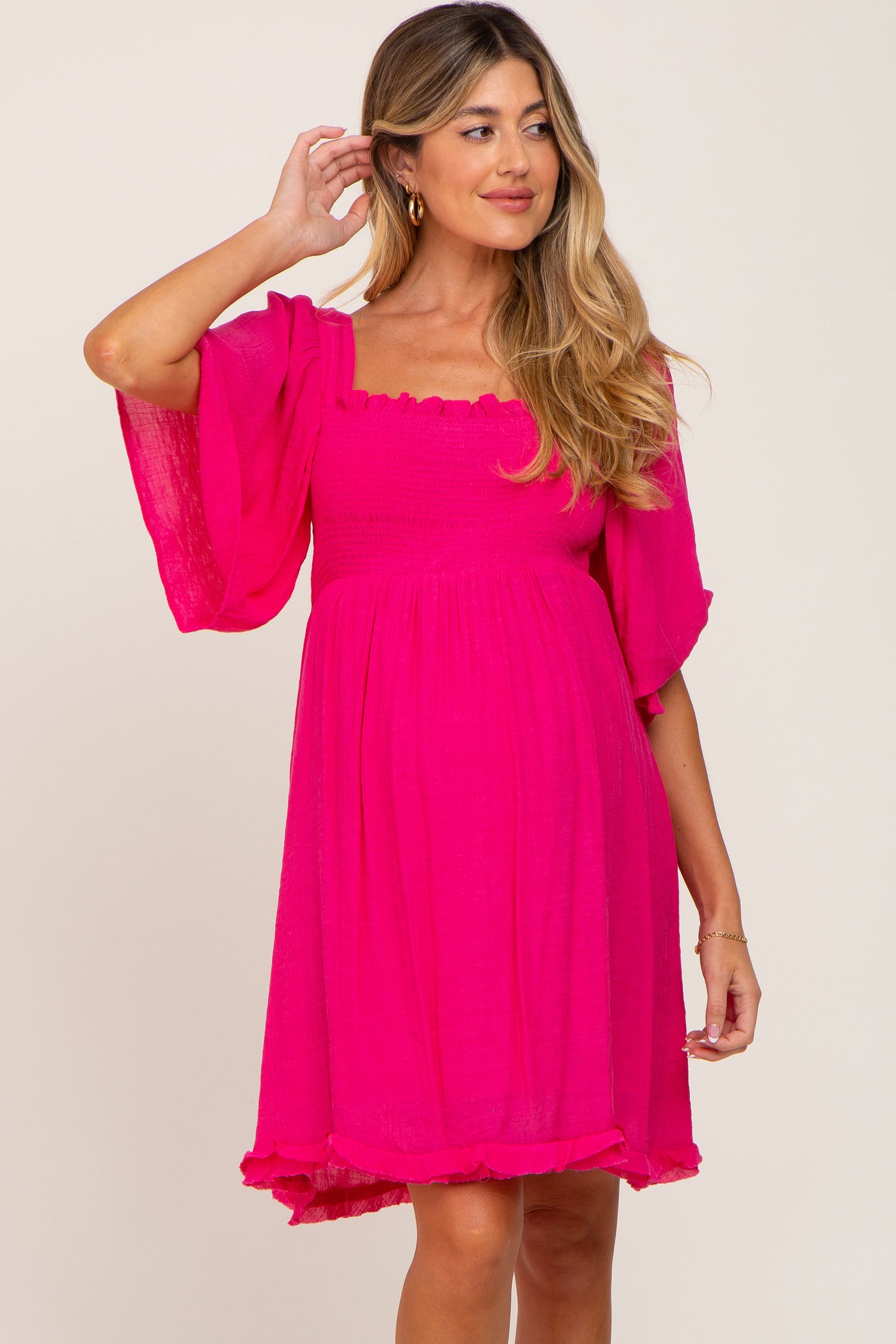 woman wearing a hot pink smocked maternity dress with flutter sleeves and a square neckline