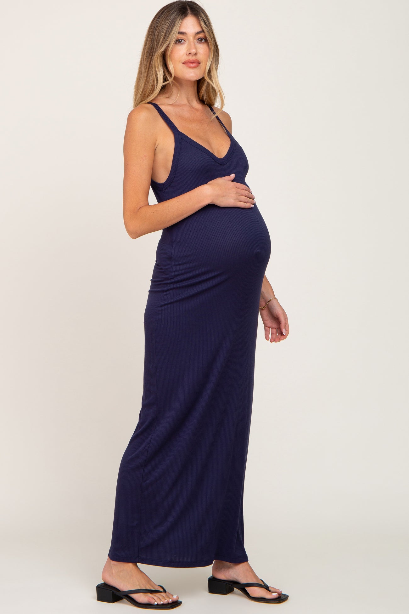 Pregnant woman wearing a navy blue ribbed maternity maxi dress with spaghetti straps and black sandals