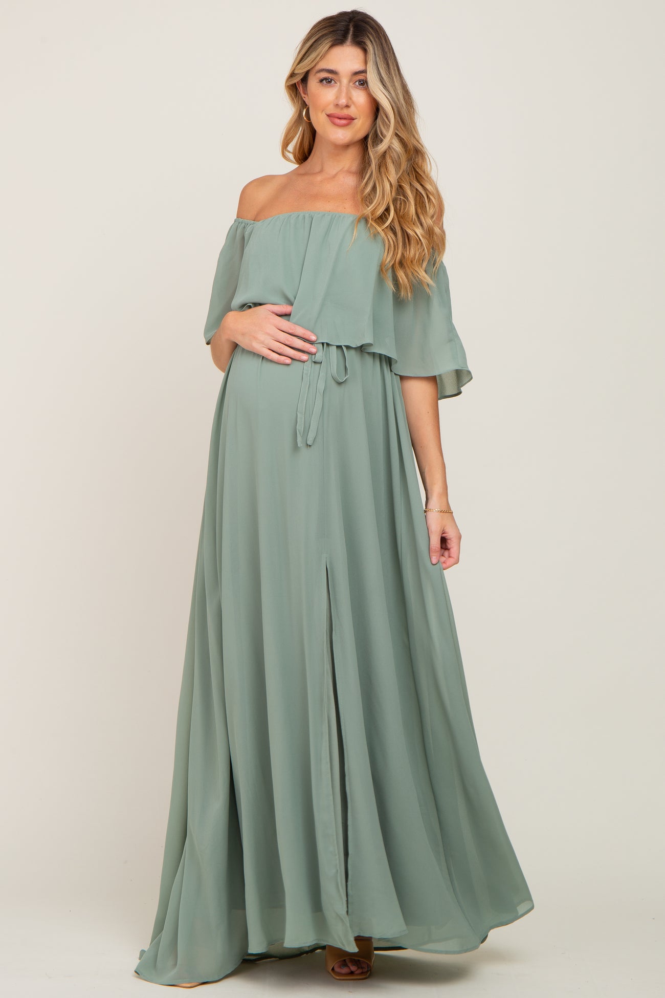 Pregnant woman wearing a sage green off-the-shoulder maternity maxi dress with a ruffled bodice and front slit