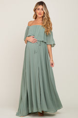 Pregnant woman wearing a sage green off-the-shoulder maternity maxi dress with a ruffled bodice and front slit