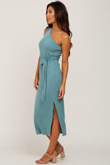 woman wearing a light blue one shoulder ribbed midi dress with a waist tie and side slit