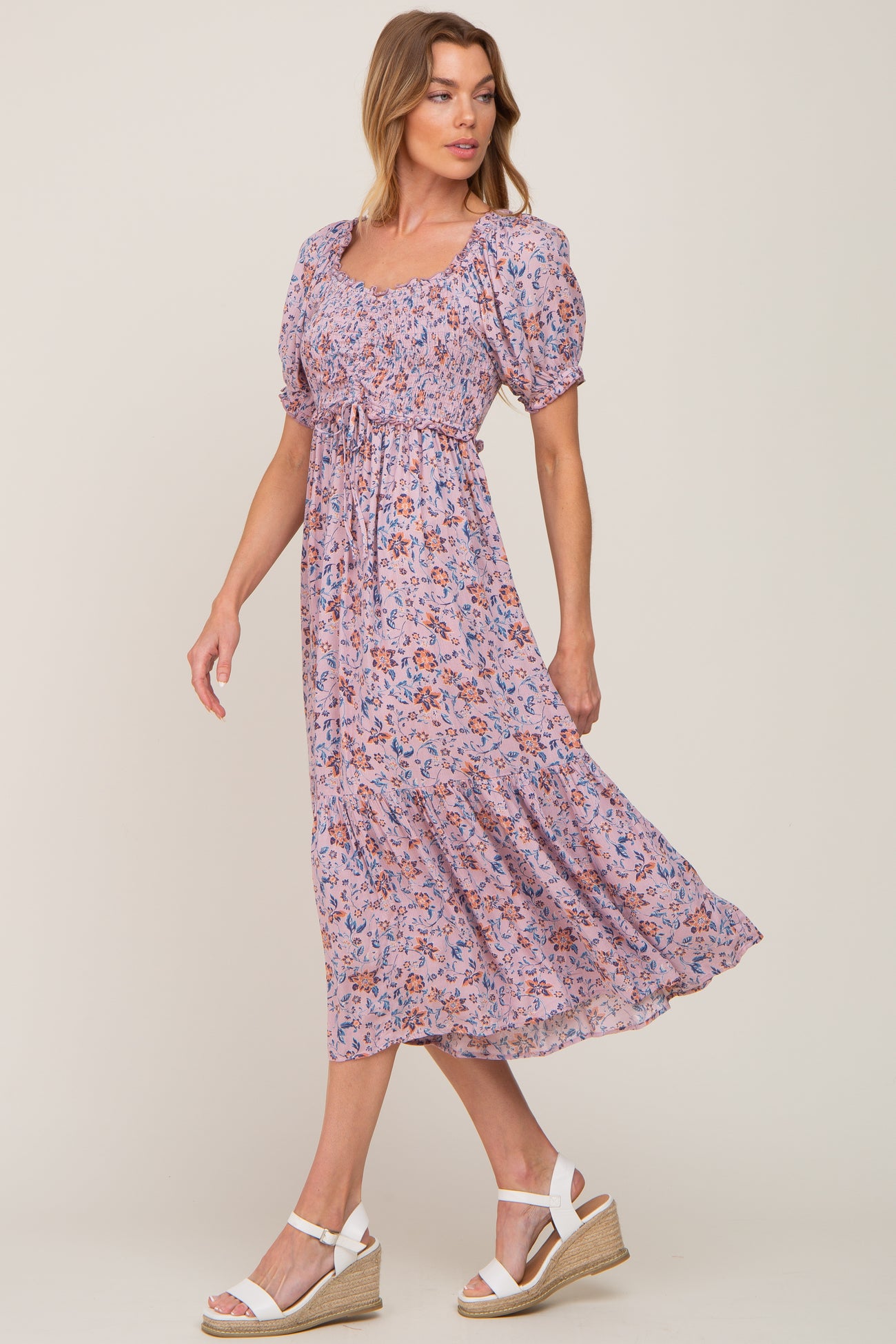woman wearing a lavender floral smocked midi dress with puff sleeves and white wedge sandals