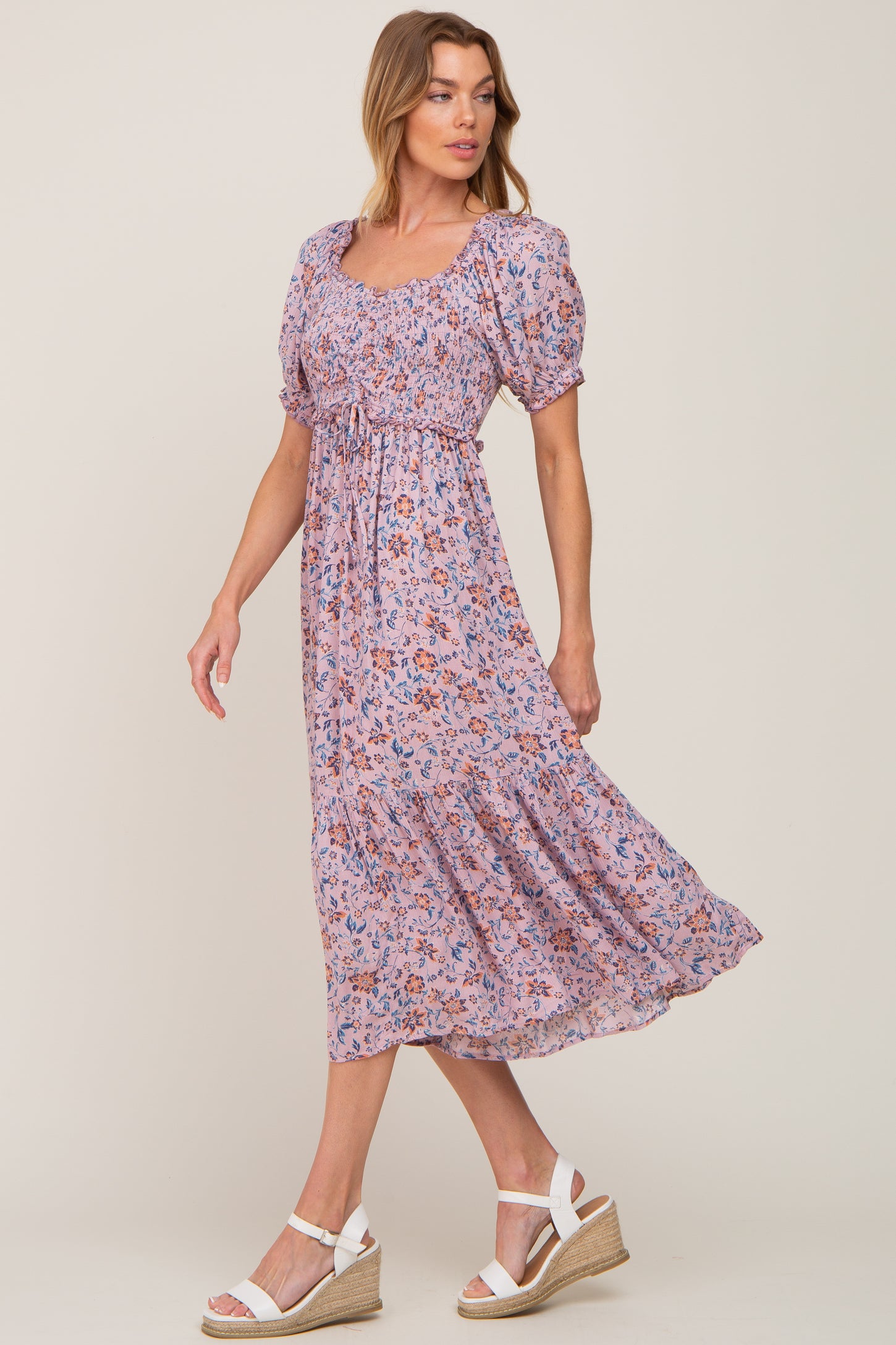 woman wearing a lavender floral smocked midi dress with puff sleeves and white wedge sandals