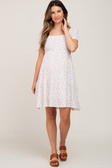 woman wearing a white floral maternity dress with puff sleeves and brown sandals