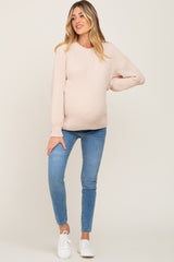 pregnant woman wearing a cream ribbed maternity sweater and blue skinny jeans with white sneakers
