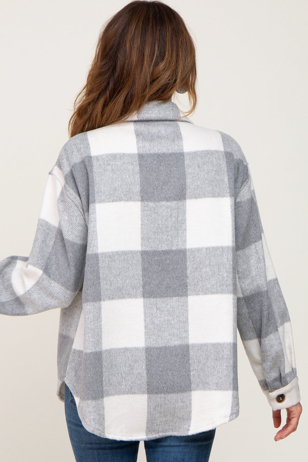 Back view of a woman wearing a grey and white buffalo plaid flannel shirt jacket with blue jeans