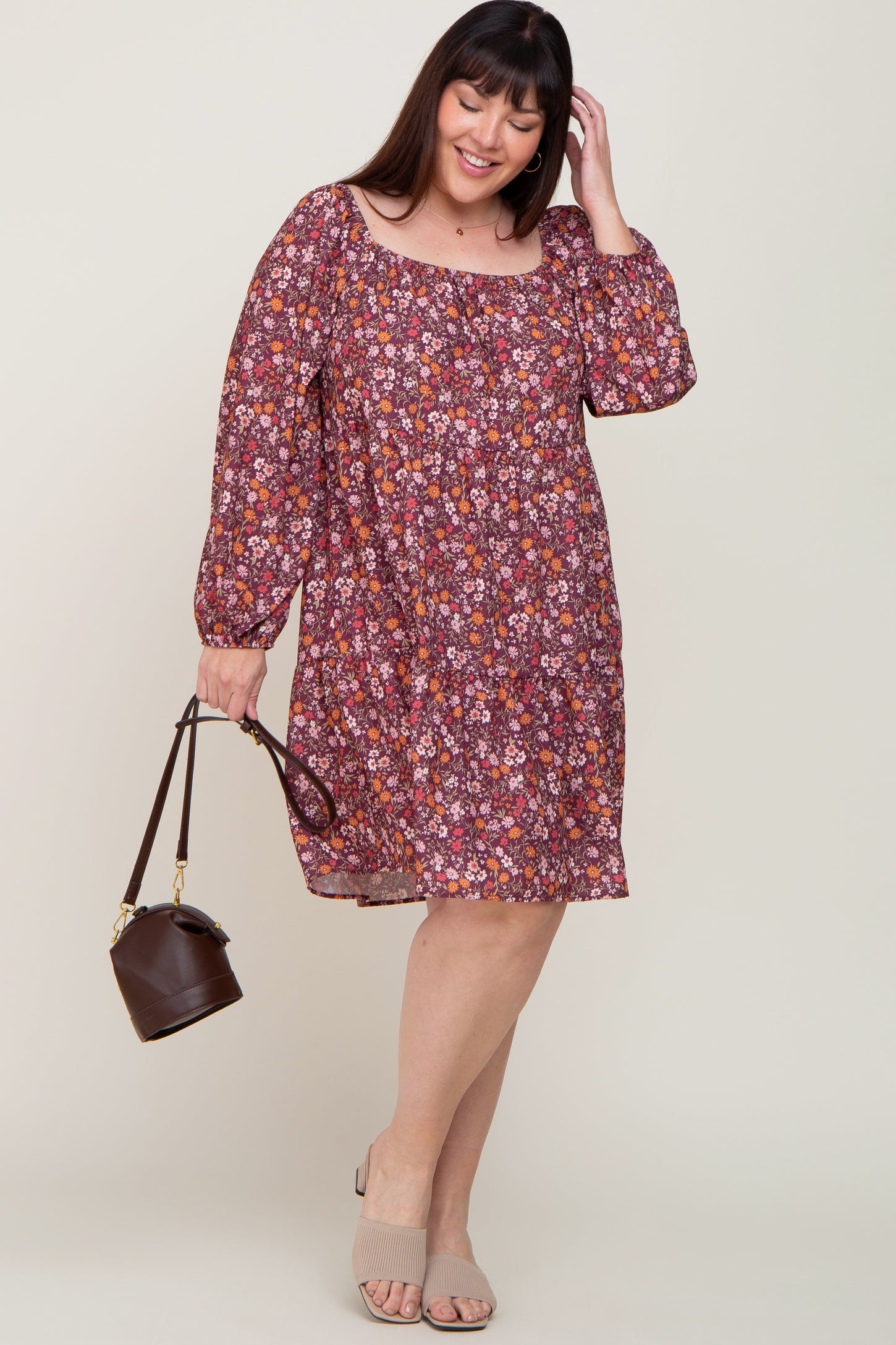 smiling woman in plus size floral long sleeve tiered dress holding a brown bucket bag