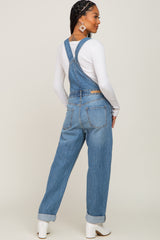 Woman wearing blue denim overalls and a white long sleeve shirt with white boots seen from the back