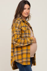 Pregnant woman wearing a yellow plaid flannel shirt and tan maternity top holding her baby bump