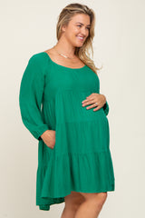 woman wearing a green long sleeve maternity dress with tiers and pockets, gently holding her baby bump