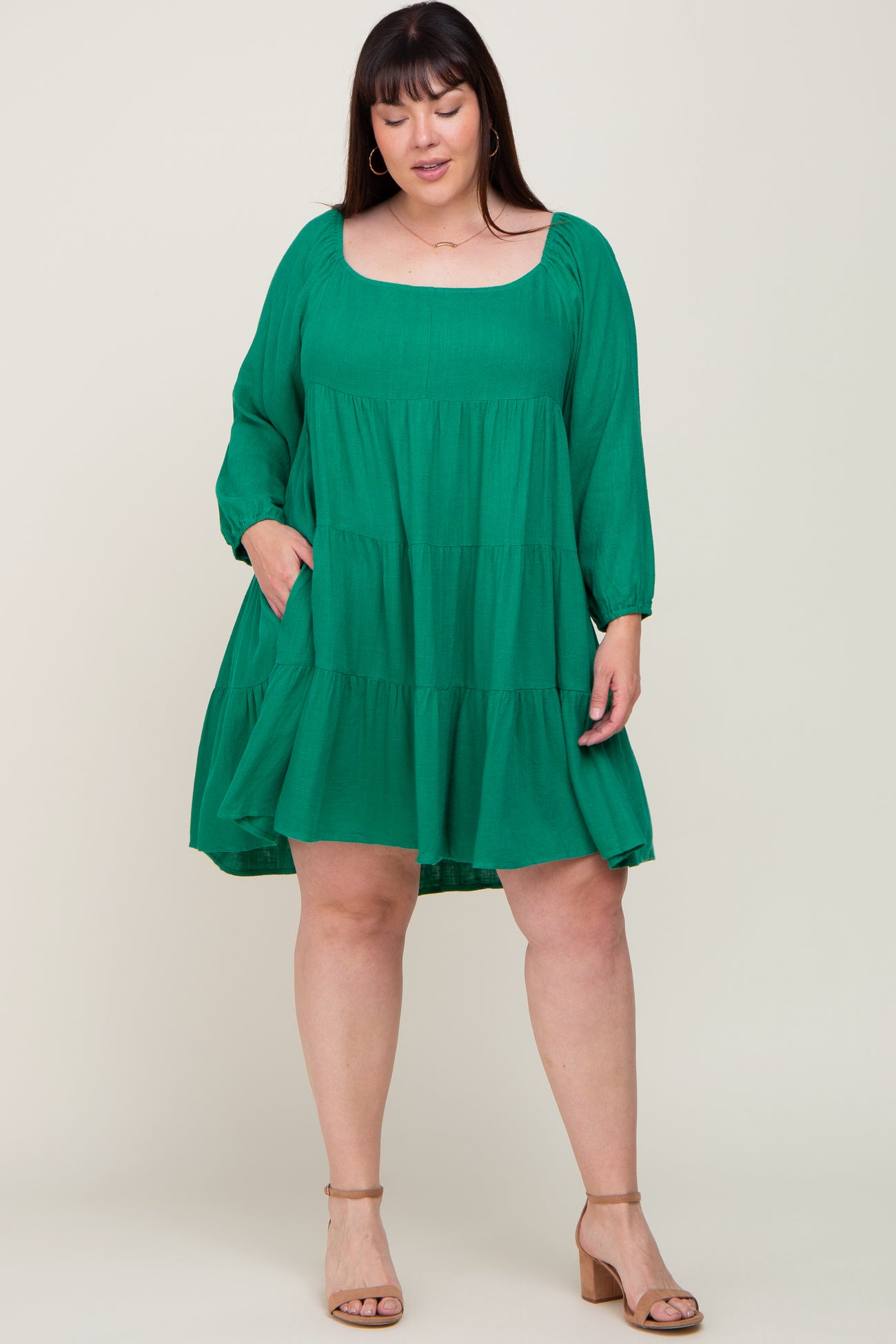 woman wearing a green tiered babydoll dress with long sleeves and square neckline, standing with hands in pockets