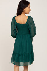 Back view of a woman wearing a dark green smocked mini dress with long sheer puff sleeves and metallic stripes