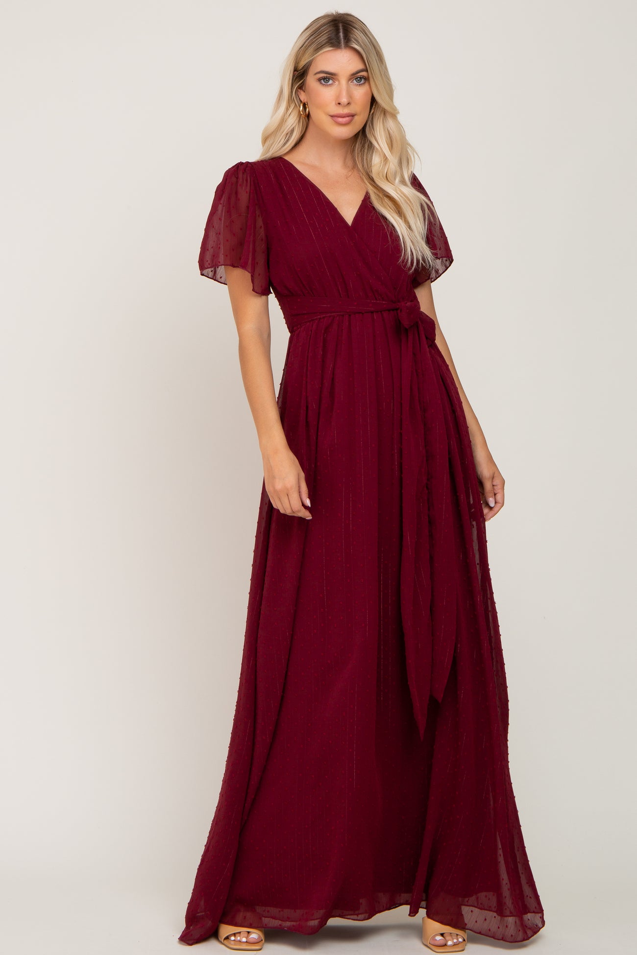 woman wearing a burgundy short sleeve wrap maxi dress with a waist tie and gold hoop earrings