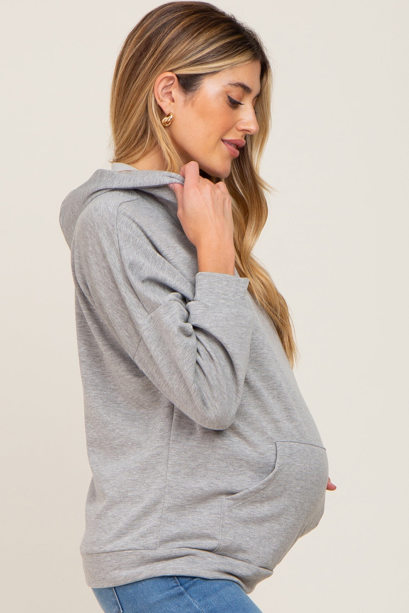pregnant woman wearing a grey maternity hoodie and blue jeans in a side profile view