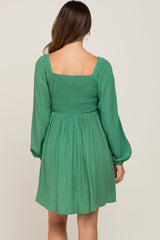 Back view of a woman wearing a green long sleeve mini dress with a smocked bodice and square neckline