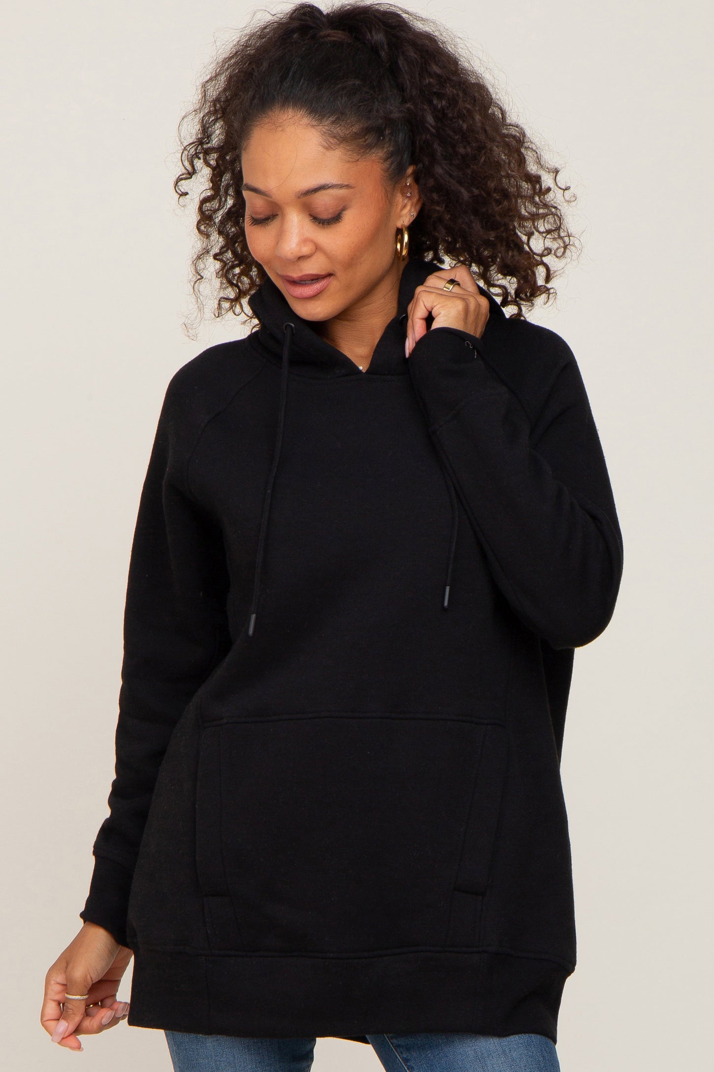 woman with curly hair wearing a black pullover hoodie with a front pocket and drawstrings