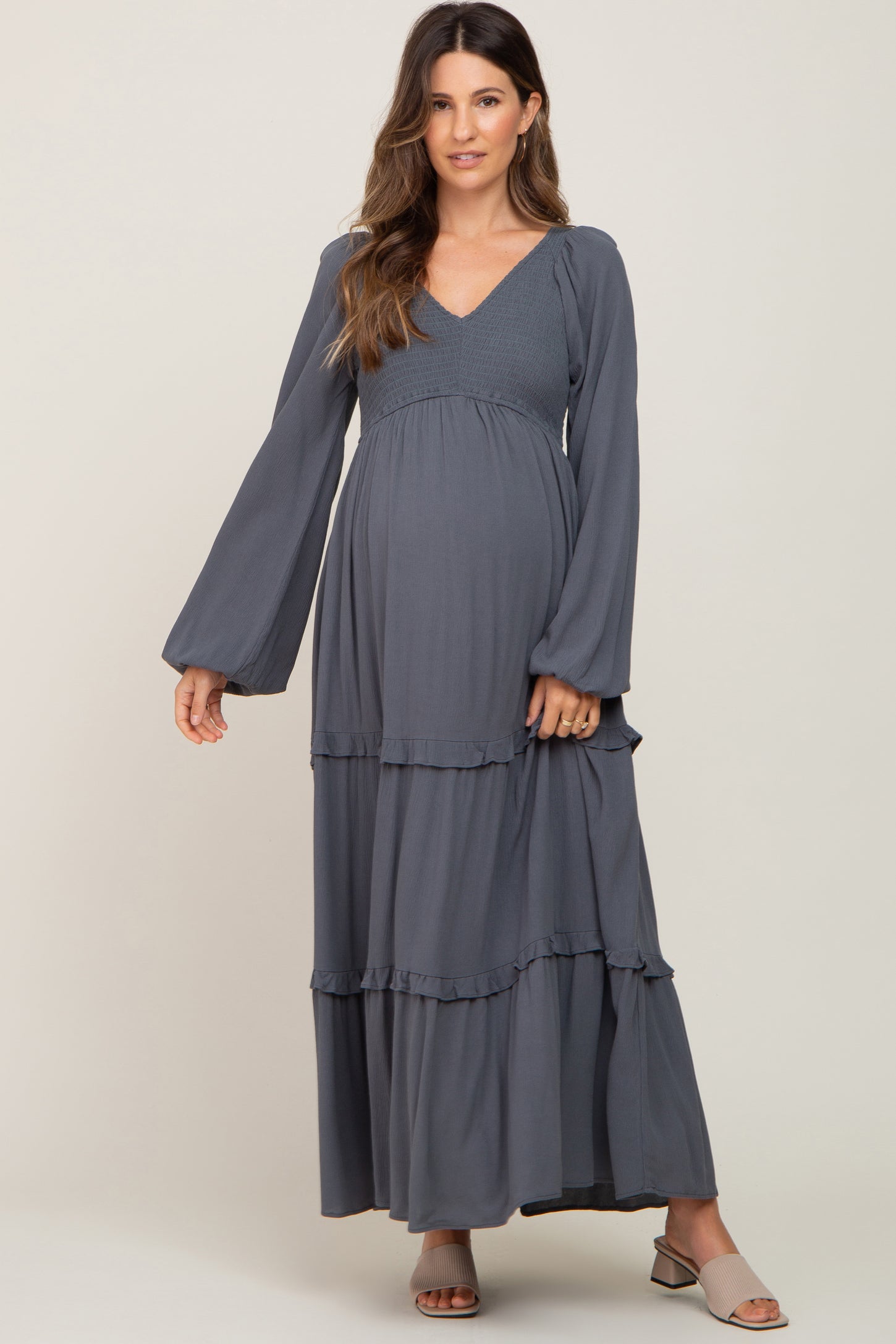 Pregnant woman wearing a charcoal grey long sleeve tiered maternity maxi dress with smocked bodice