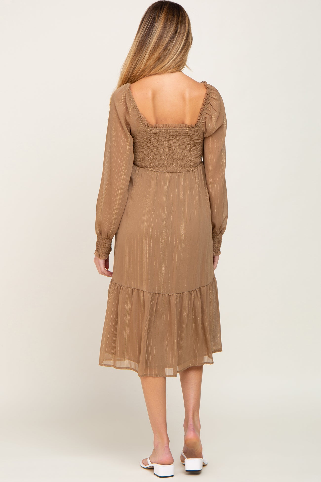 Back view of a woman wearing a brown long sleeve smocked midi dress with gold metallic pinstripes