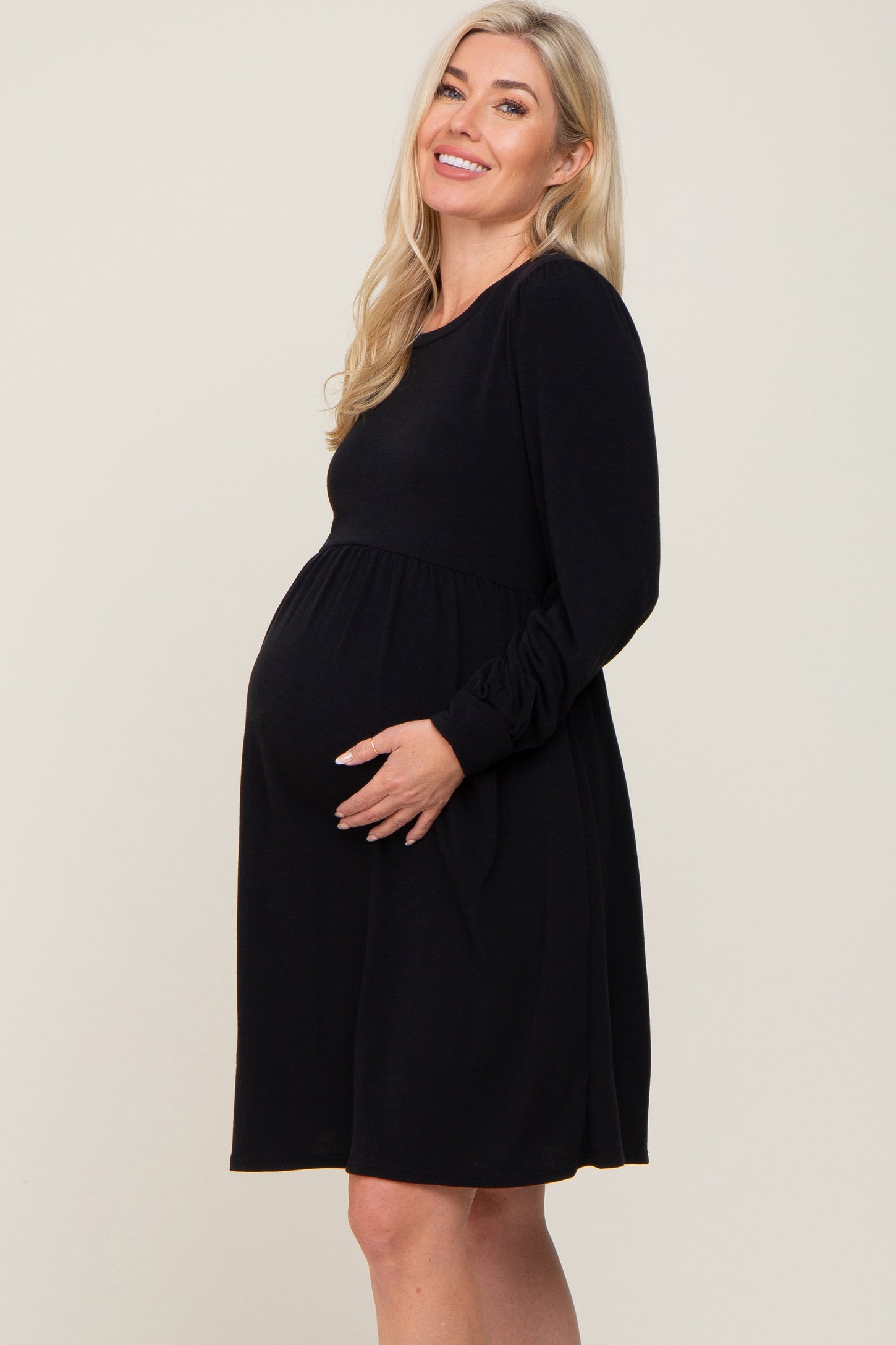 smiling pregnant woman with blonde hair wearing a long sleeve black maternity dress