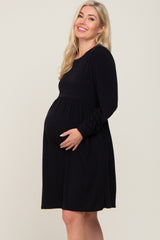 smiling pregnant woman with blonde hair wearing a long sleeve black maternity dress