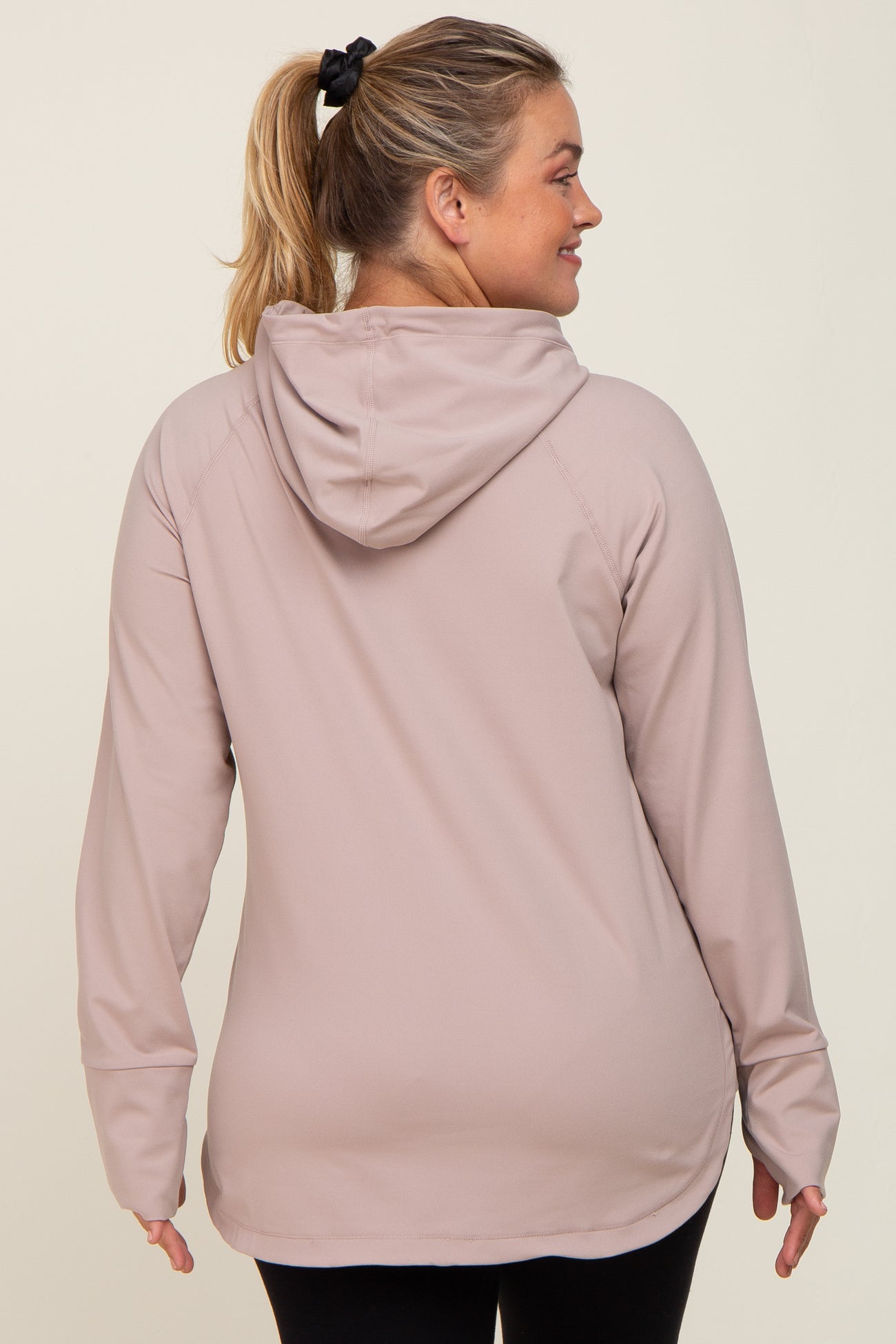 Back view of a woman wearing a mauve long sleeve hooded athletic top with thumbholes