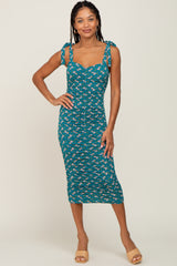 woman wearing a teal floral midi dress with tie straps and a fitted silhouette, standing and smiling