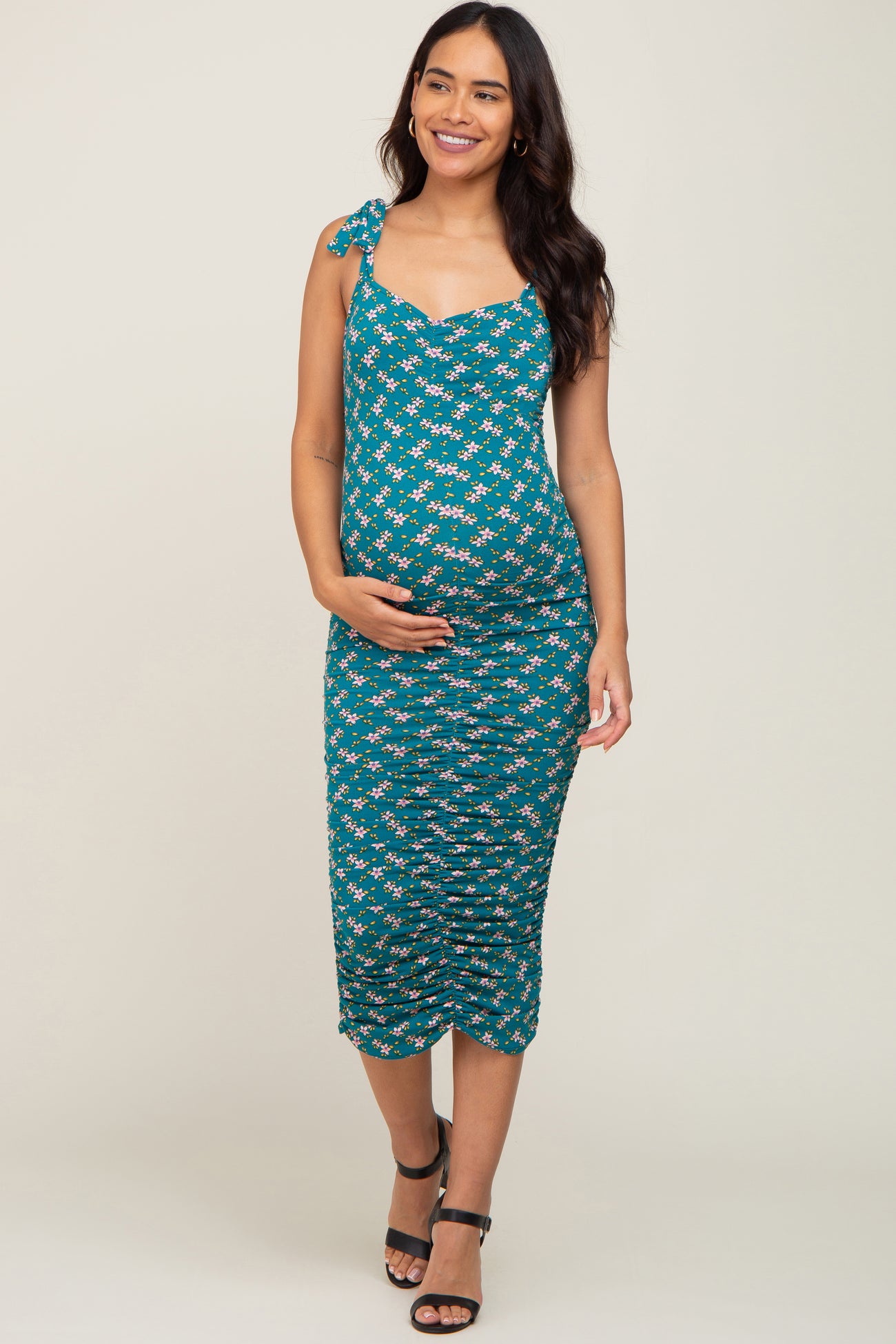 woman wearing a teal floral maternity dress with adjustable straps and a fitted silhouette, showcasing her baby bump