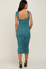 woman wearing a teal maternity dress with floral print and tie shoulder straps, showing a fitted silhouette
